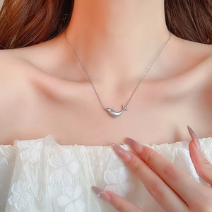Detail of matte silver dolphin pendant necklace worn with a white lace top