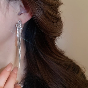 Macro shot of silver bow knot earrings with dangling crystal tassels on female model