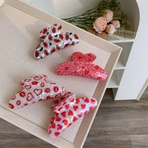 Detail of red heart and lip print hair claws on a beige linen tray in a soft setting