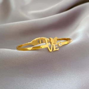 Close-up of golden butterfly bracelet with LOVE engraving and sparkling zircon stone