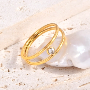 Minimalist double-layer gold ring with clear zircon on textured stone background