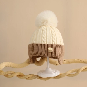 Detail of baby winter knit hat with cable pattern, dual-tone colors and large fur pompom