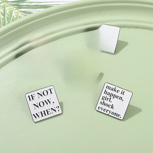 Minimalist white enamel pins set with black inspirational quotes on a green tray