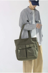 Detailed view of an olive green canvas tote bag with large front pockets worn on shoulder