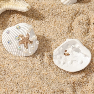 Detailed view of shell earrings with gold starfish, white pearls and colorful rhinestones