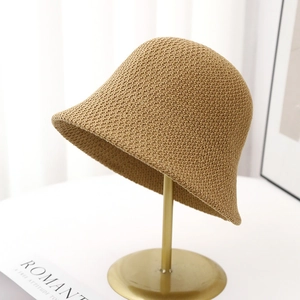 Detailed close-up of khaki woven straw bucket hat on a gold stand with a cozy backdrop
