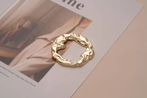Detail shot of irregular textured gold metal buckle accessory on a beige background