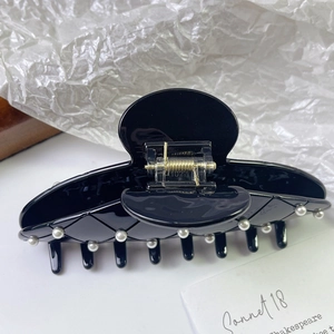 Close-up of black glossy acetate hair claw clip with lattice pattern and pearls