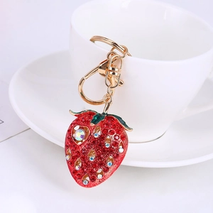 Detailed close-up of a red strawberry keychain with crystals on a white ceramic dish