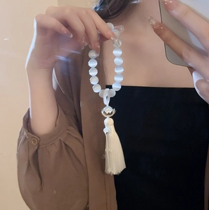 Detailed view of white cat-eye bead bracelet with silver lotus and silk tassel charm