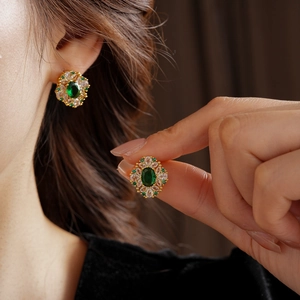 Détail de boucles d'oreilles dorées avec pierres ovales vertes et cristaux brillants