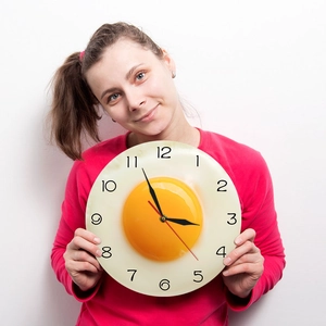 Modern 3D fried egg wall clock with Arabic numerals held by a person on white background