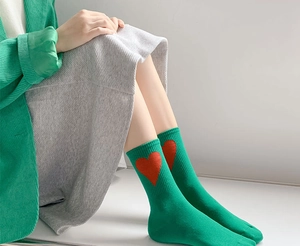 Detail of green mid-calf crew socks featuring red heart pattern and ribbed knit cuffs