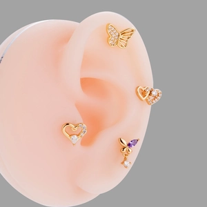Macro view of gold heart and butterfly ear studs with zircons on a silicone ear model