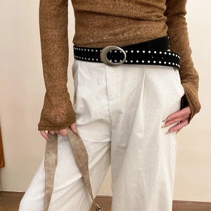Détail de ceinture en cuir noir avec rivets argentés et boucle ovale sur un pantalon blanc