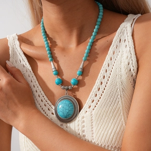 Detailed close-up of a bohemian turquoise beaded necklace on a white woven top