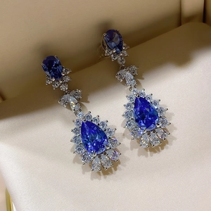 Detailed view of teardrop blue rhinestone earrings with luxury halo setting on fabric