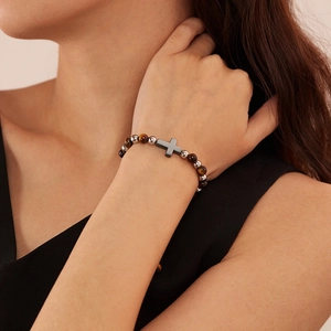 Primo piano di un bracciale da uomo con pietre occhio di tigre e ciondolo a croce nera
