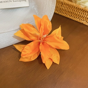 Close-up of a realistic orange fabric lily hair clip on a natural wooden surface