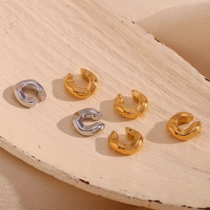 Close-up of minimalist gold and silver C-shaped ear cuffs on a white tray with silk