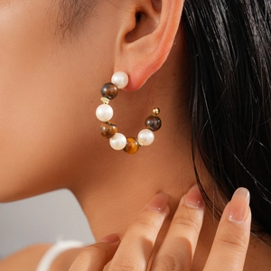 Close-up of C-shaped hoop earrings with brown tiger eye beads and white pearls on model