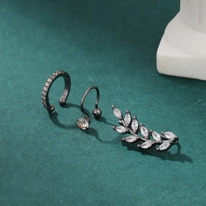 Three-piece gunmetal leaf ear cuff set with sparkling zircons on textured green surface