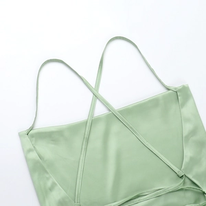 Detail of light green satin dress featuring thin cross-back straps and smooth silk texture