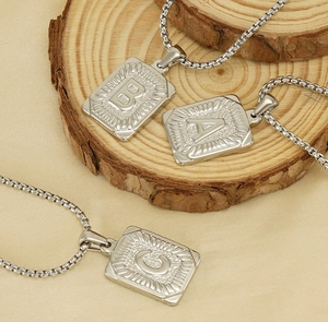 Detailed macro view of square silver initial pendants A, B, C on a pearl chain