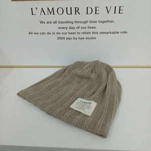 Detail of cable knit beanie with brand patch and textured khaki yarn finish