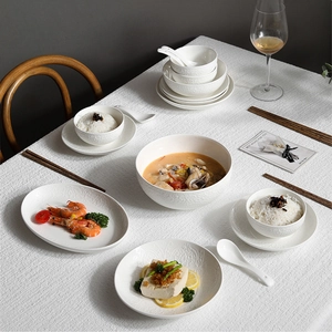 Elegant white ceramic tableware set with embossed patterns on white tablecloth