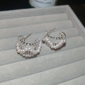 Detail of silver C-shaped pearl hoop earrings inside a velvet jewelry display box