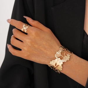 Détail de la bague et du bracelet dorés en forme de feuille de ginkgo évidée sur fond noir