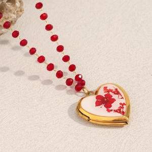 Macro detail of 18K gold-plated heart locket necklace with red pressed flower and beads