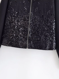 Detailed close-up of shiny sequins and silver metal zipper on a black casual jacket