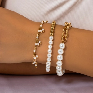 Detailed view of layered faux pearl and gold chain bracelets set on a female wrist