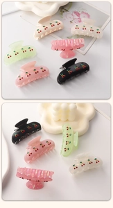 Detail showing colorful resin hair claws with embroidered cherry patterns on a white tray