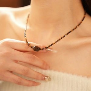 Close-up of tiger eye beaded necklace with brown rectangular stone on a model's neck