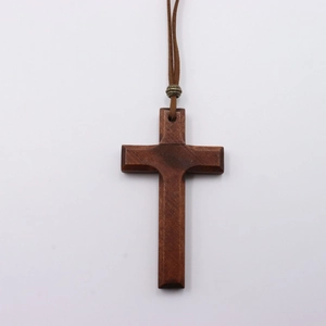 Close-up of a dark brown wooden cross pendant with natural texture and a bronze bead