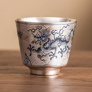Taza de té plateada con motivo de dragón azul y ondas sobre mesa de madera