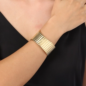 Detailed view of wide gold wave-textured stainless steel cuff bracelet on wrist
