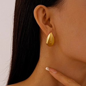 Gros plan d'une boucle d'oreille goutte dorée au fini métallique brillant sur modèle