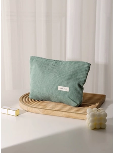 Green corduroy cosmetic bag on a wooden tray with a minimalist vertical striped design