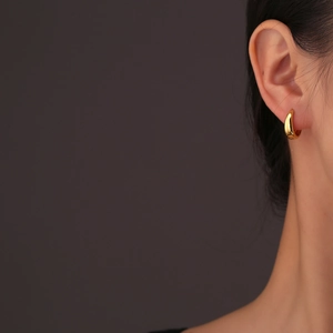 Boucles d'oreilles créoles dorées géométriques au fini poli portées par un mannequin