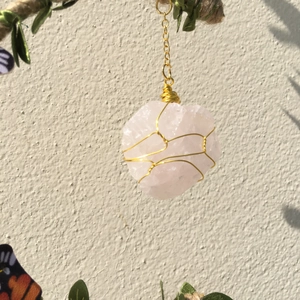 Detail of hand-wrapped rose quartz crystal pendant with golden wire and leaf accents
