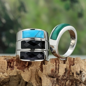 Detail showing four assorted stainless steel rings with gemstone inlays on a tree bark