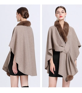 Detail of tan knit poncho featuring faux fur collar and decorative pom-poms on the hem