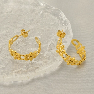 Macro detail of C-shaped gold hollow earrings with intricate vintage floral patterns