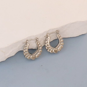 Detail of silver horseshoe earrings with embossed heart patterns on stone background