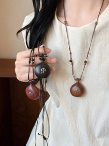 Detail of wooden gourd pendant necklace featuring an intricate metal cross inlay and beads
