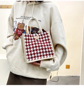 Detail of red houndstooth canvas tote bag with woven rope handle and wooden button closure